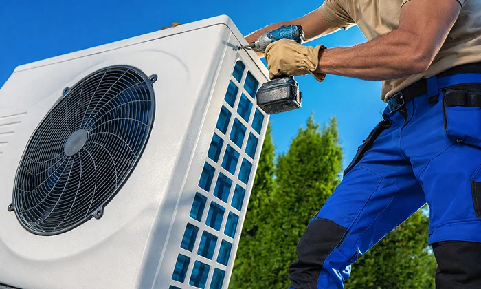 A technician using a power drill to service an outdoor AC unit