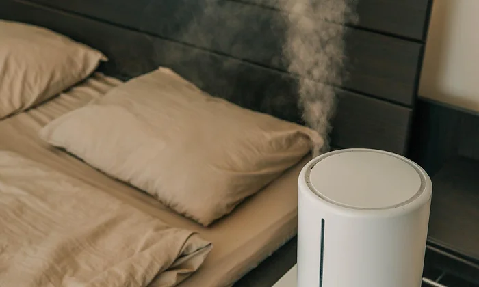 A humidifier releasing mist next to a bed in a bedroom
