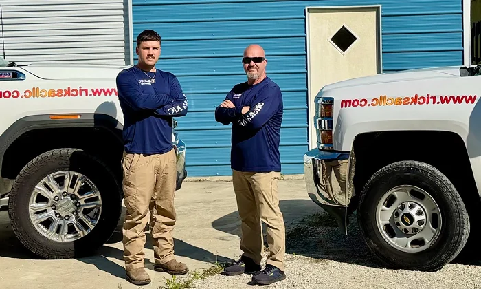 Two Rick's A/C Maintenance & Service technicians standing in front of their service trucks