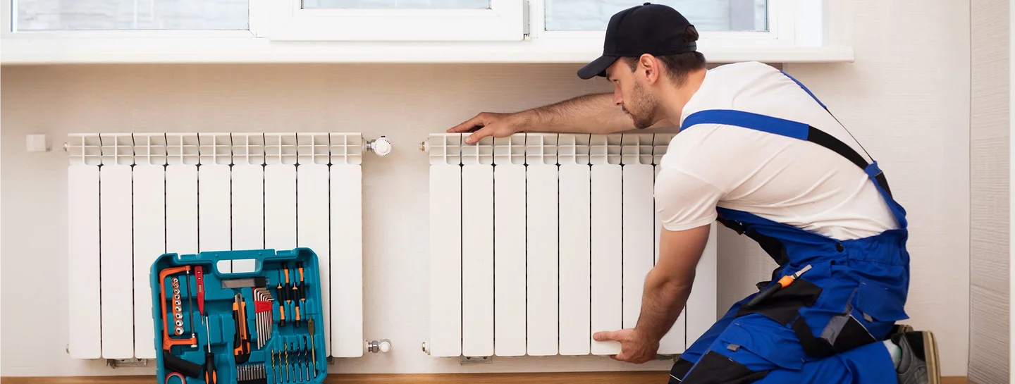 A technician installing a wall radiator with a toolbox nearby